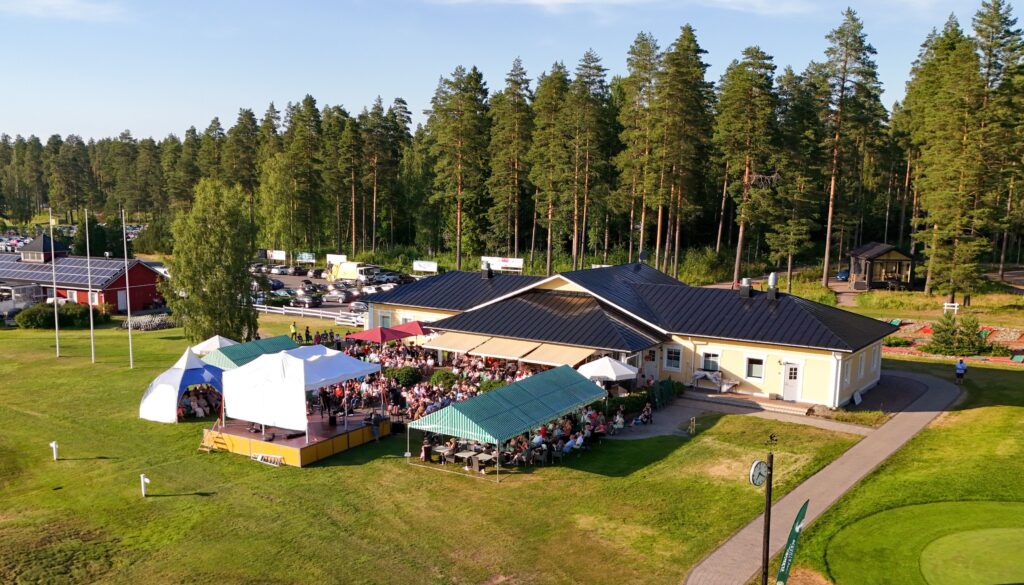 puita, rakennuksia, esiintymislava ja yleisöä katosten alla