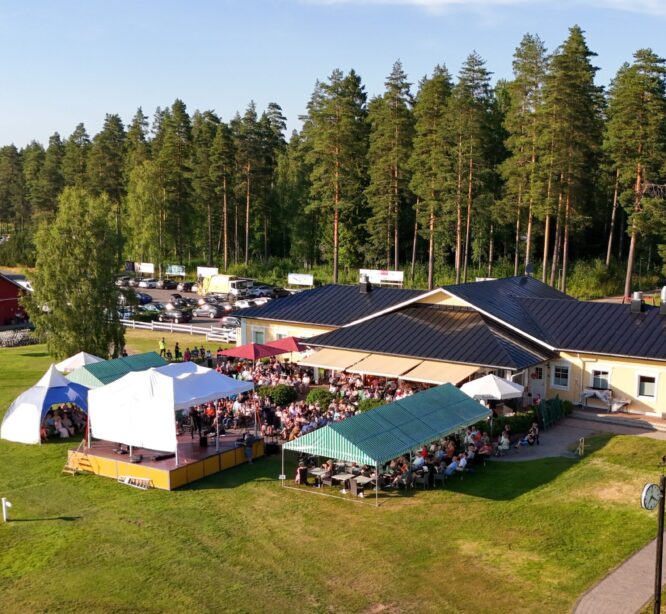 puita, rakennuksia, esiintymislava ja yleisöä katosten alla