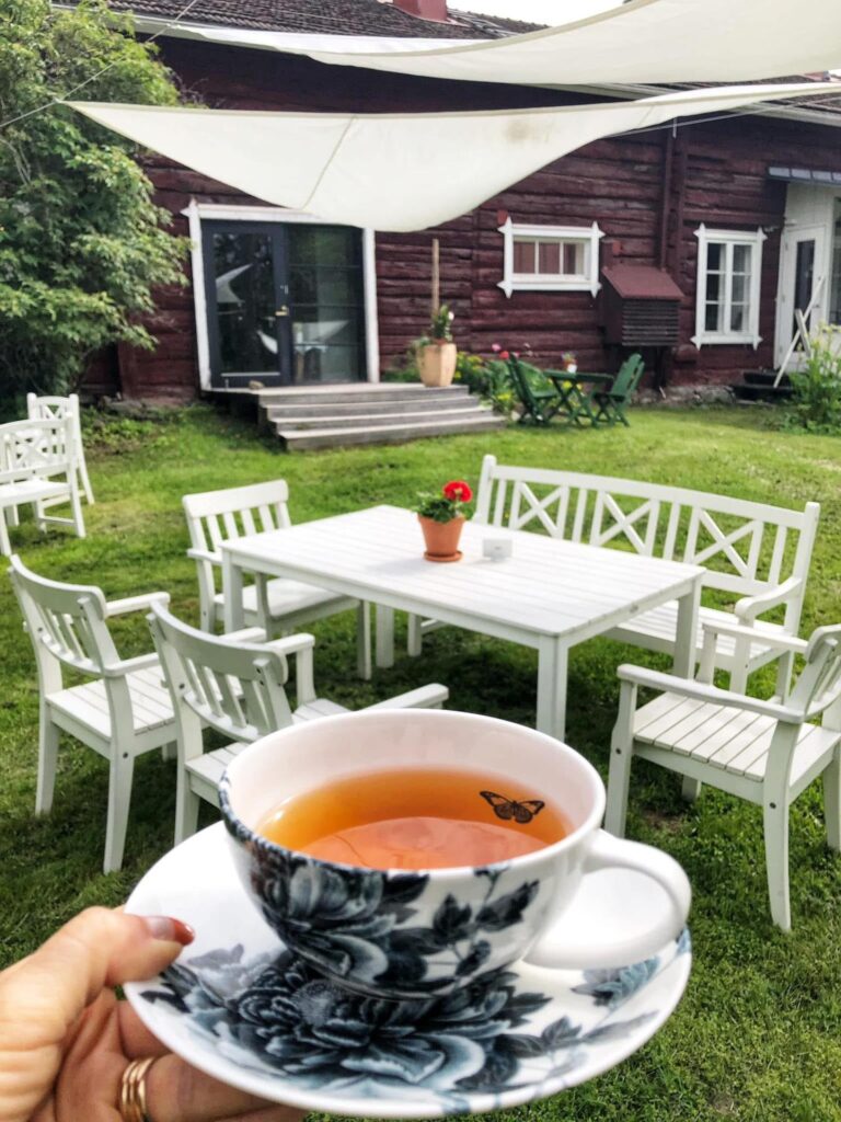 Puutarhapöytä ja käsi, joka ojentaa teetä kauniissa kupissa.