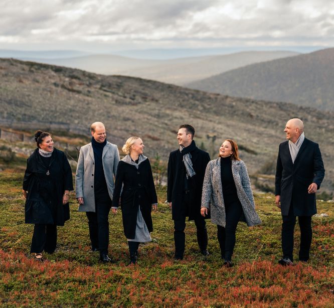 Viisi nauravaa henkilöä vuoristomaisemassa.