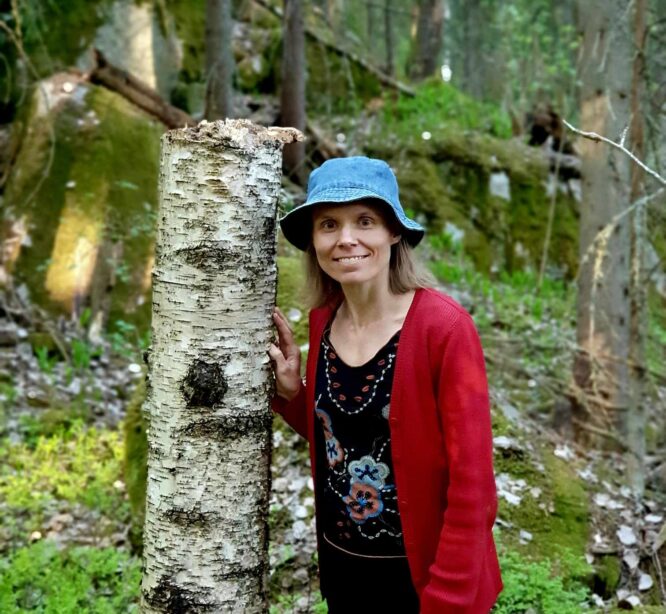 Nainen nojaa puuhun metsässä.