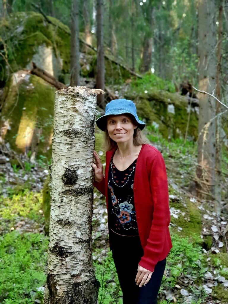 Nainen nojaa puuhun metsässä.